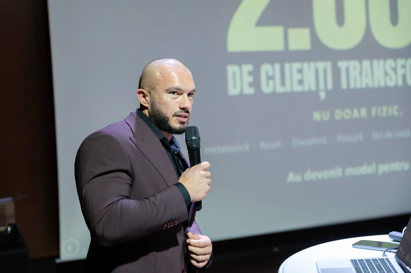 Andrei Ivan vorbește la microfon, în fața unui slide cu rezultatele clienților Ivan’s Challenge.