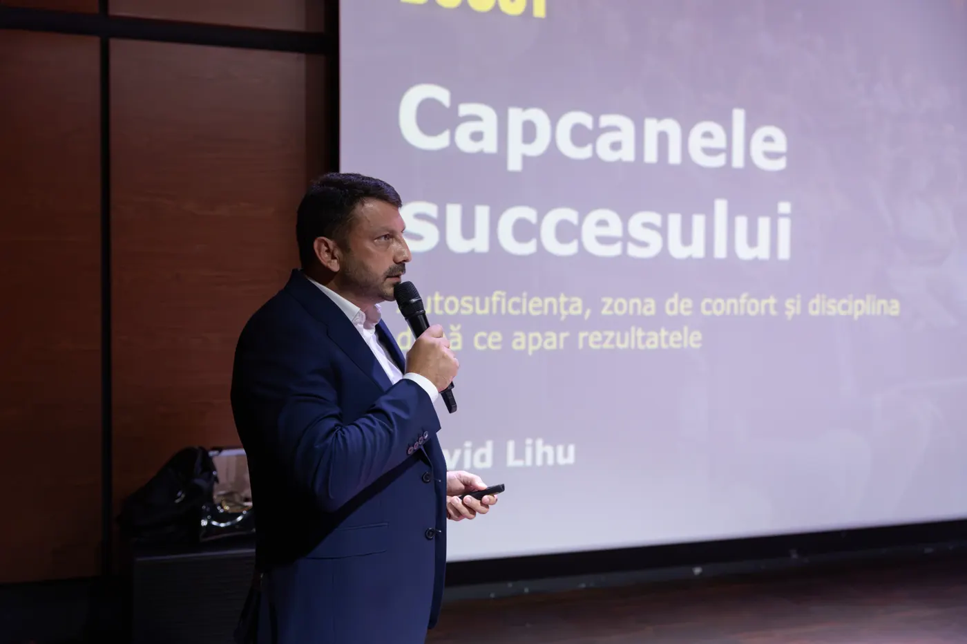 David Lihu vorbește la microfon în fața slide-ului „Capcanele succesului”.